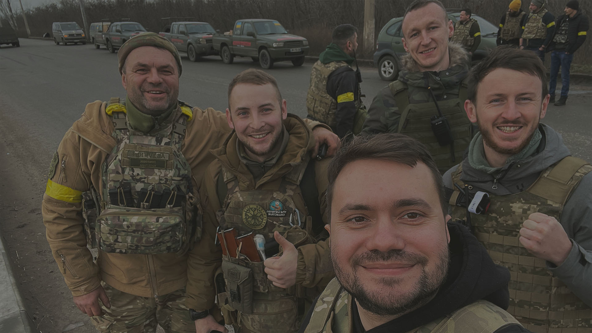 Car for Ukraine volunteers making a selfie with grateful Ukrainian soldiers, behind them are donated cars. 