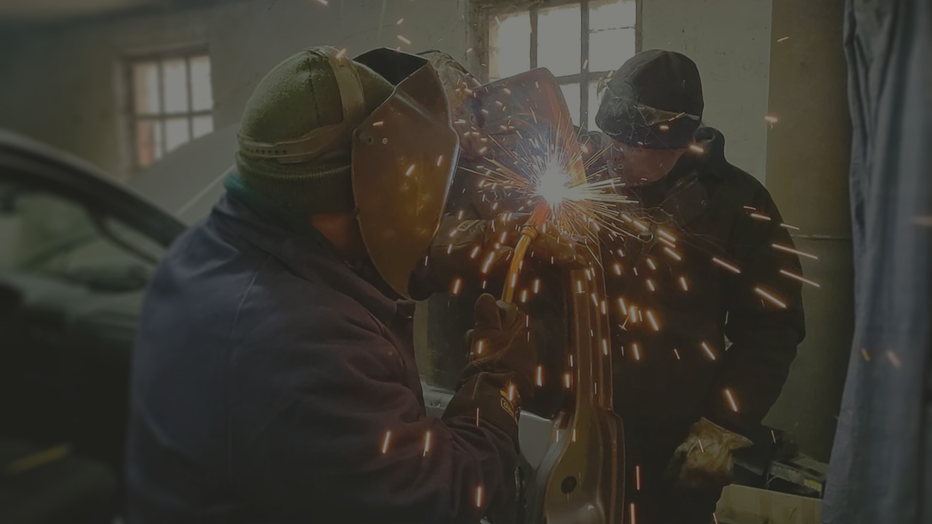 Two volunteers welding armor on the side door of a donated car.